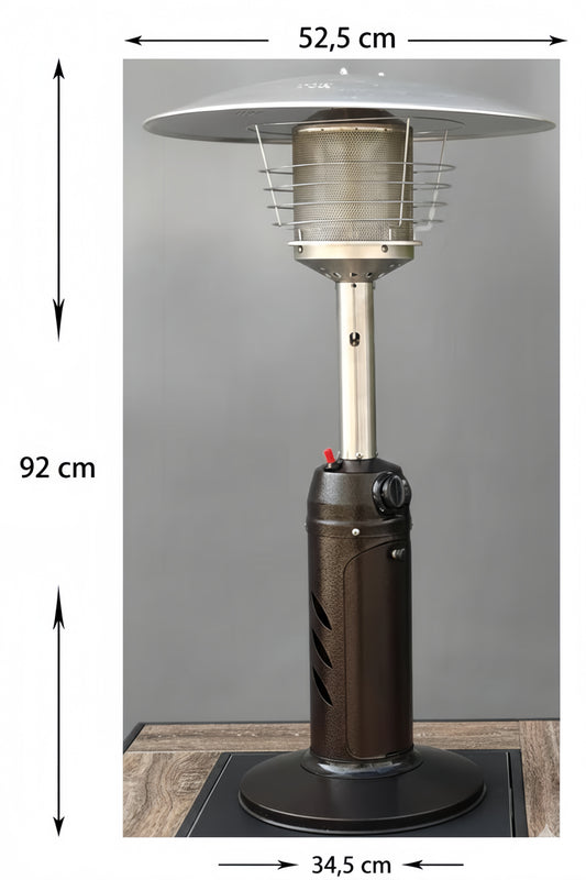 Photographie en studio d'un parasol chauffant de table au design compact, posé sur une surface boisée devant un fond gris neutre. L'appareil se compose d'un socle circulaire noir, d'un corps cylindrique en métal texturé marron foncé avec des fentes d'aération, d'un mât en acier brossé et d'un brûleur supérieur protégé par une grille et surmonté d'un réflecteur bombé argenté.