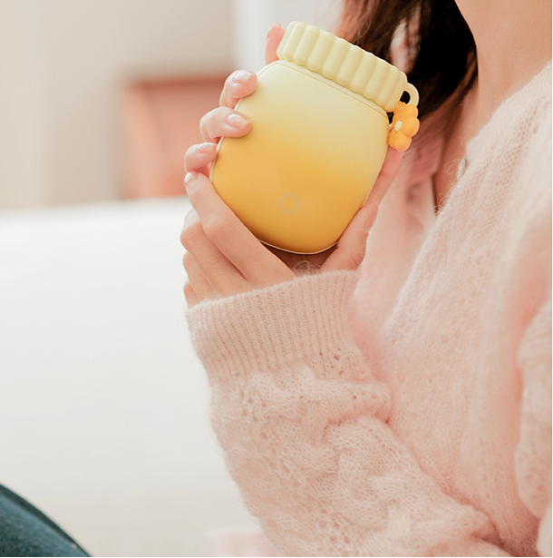 Main tenant le chauffe-main Pétale pour illustrer son ergonomie et praticité pour chauffer le cou.