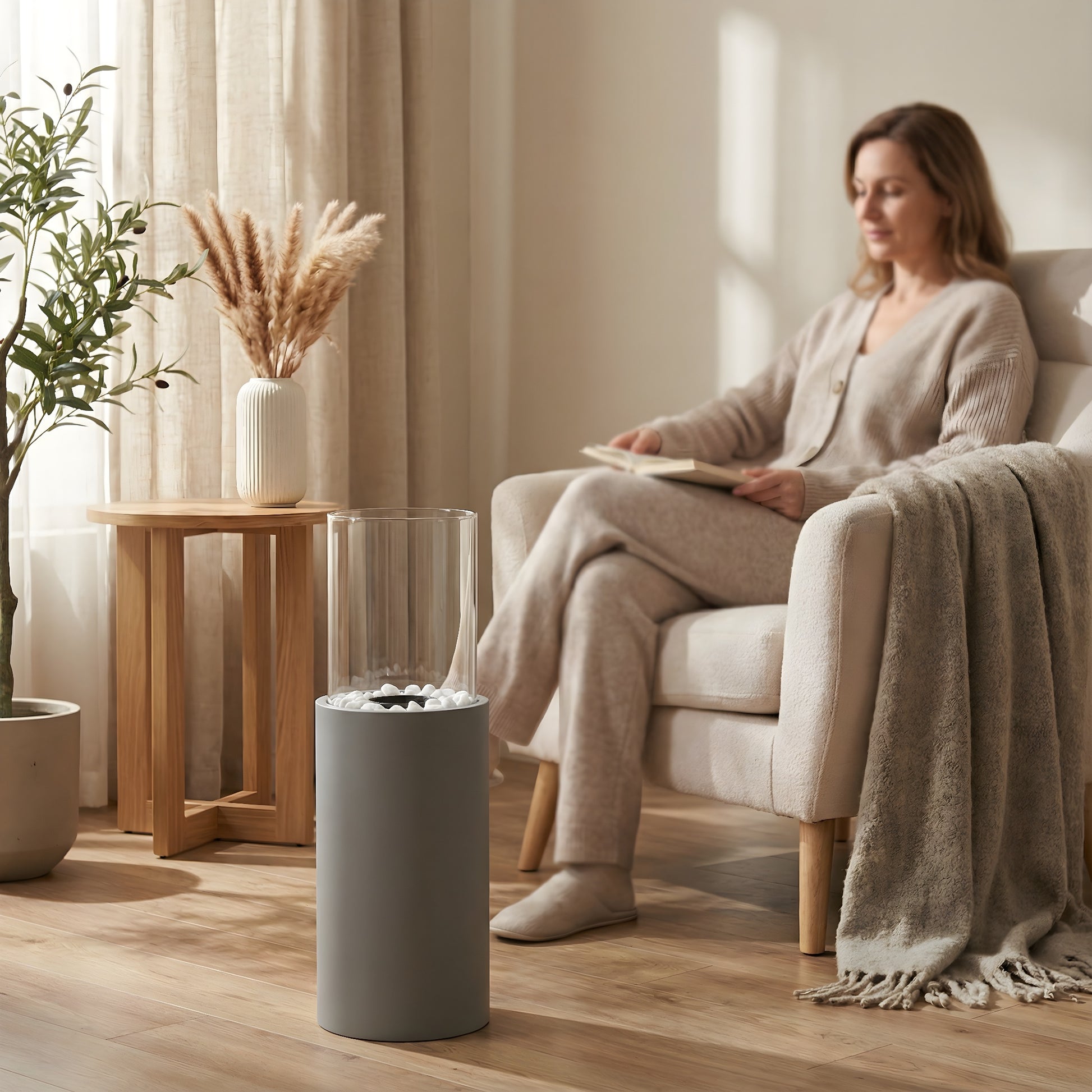 Cheminée éthanol cylindrique Calora Home dans un salon cosy, femme assise dans un fauteuil, ambiance chaleureuse et lumineuse