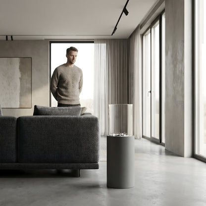 Cheminée éthanol cylindrique Calora Home dans un salon moderne et épuré, homme debout près du canapé