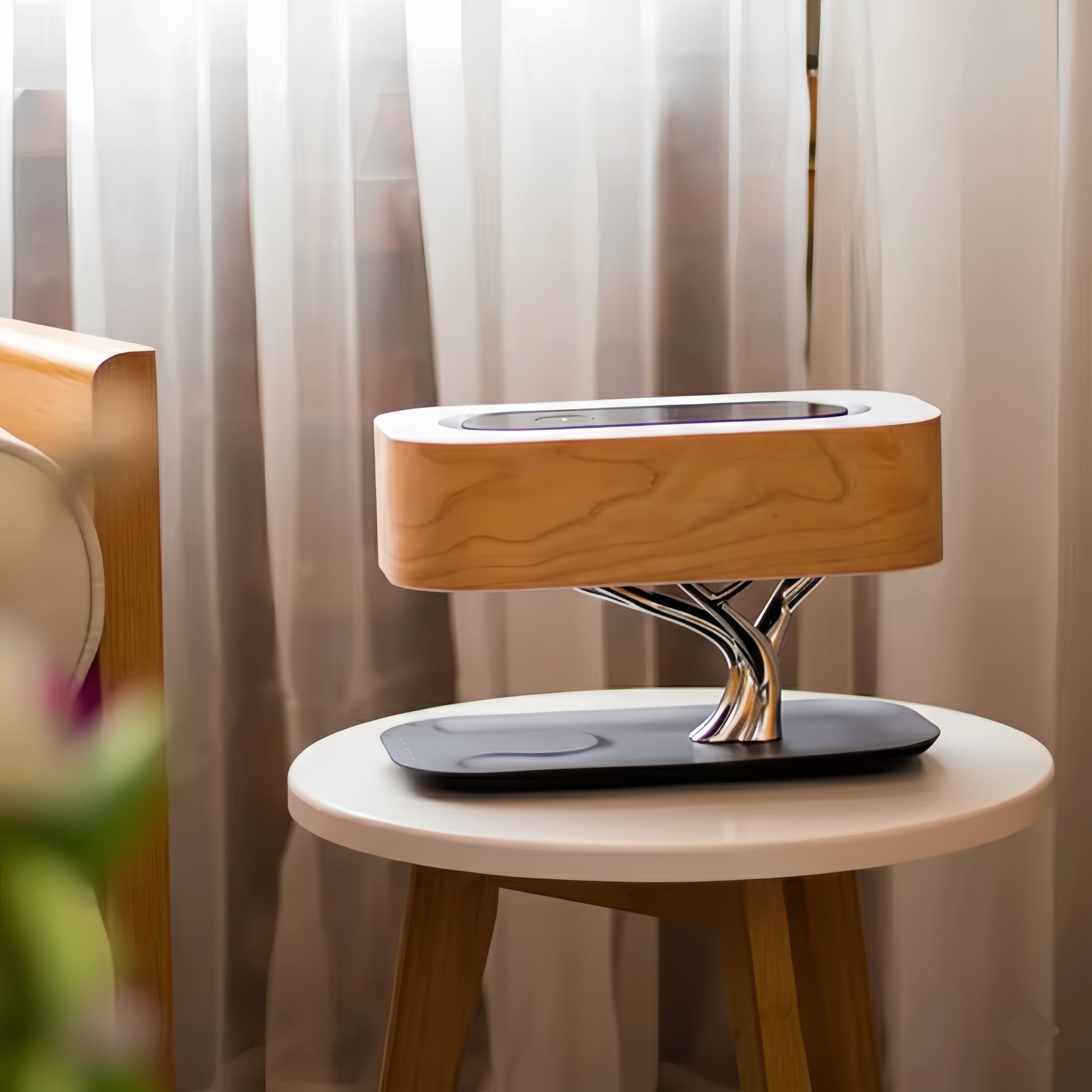 Lampe de table design avec abat-jour rectangulaire en bois clair, support argenté en forme d'arbre sur une petite table d'appoint, rideaux en arrière-plan.