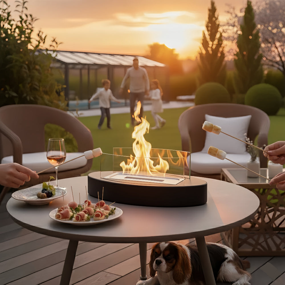 Cheminée de table ovale noire à l'éthanol avec flamme, adaptée aux soirées guimauves en extérieur sur une terrasse, avec famille et chien.